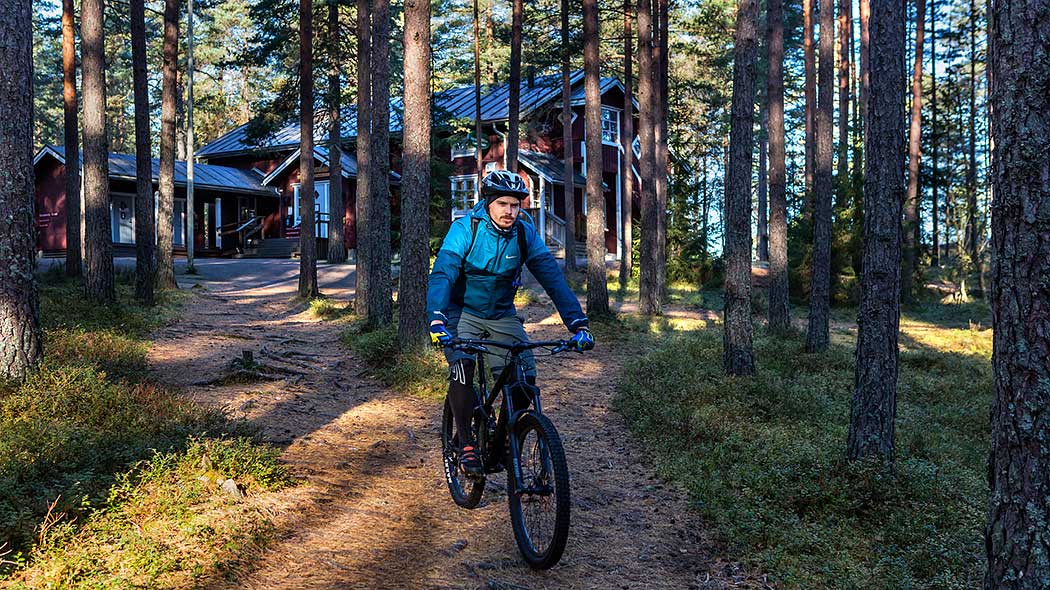 Pyöräilijä metsäpolulla. Taustalla luontokeskuksen rakennus. Teijon kansallispuisto. Kuva: Jari Kostet.