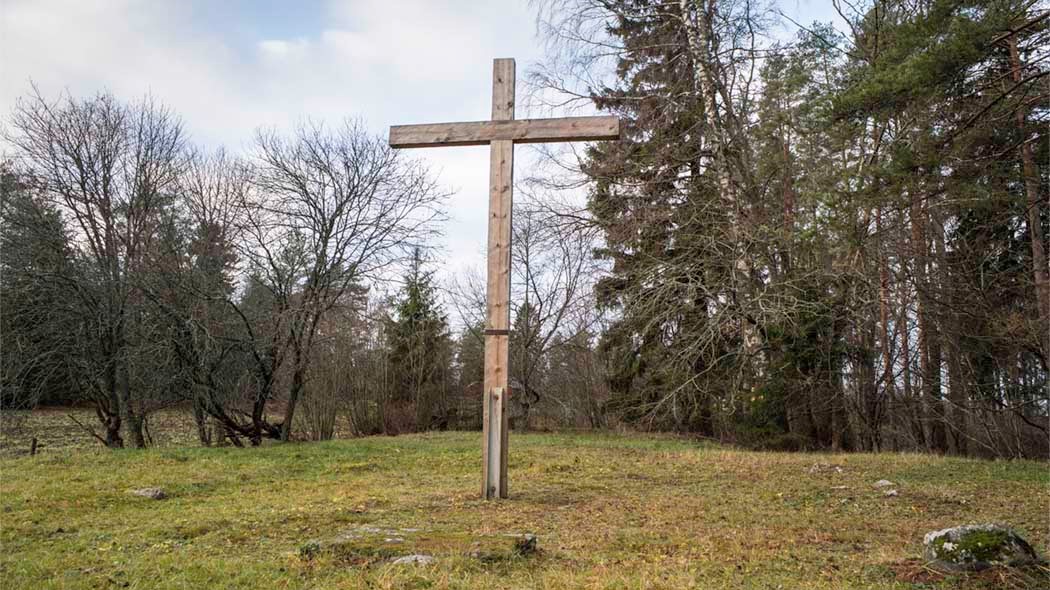 Suuri puuristi nurmella. Taustalla metsää. Ristinpelto. Kuva: Tuija Warén.