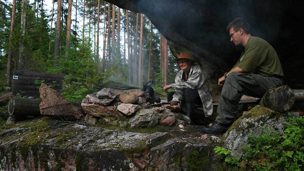 Kaksi retkeilijää tulentekopaikalla lippamaisen kivimuodostelman alla.